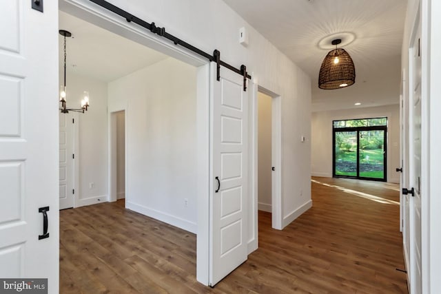 hallway with a notable chandelier, dark hardwood / wood-style floors, and a barn door