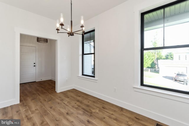 unfurnished dining area with wood-type flooring and an inviting chandelier