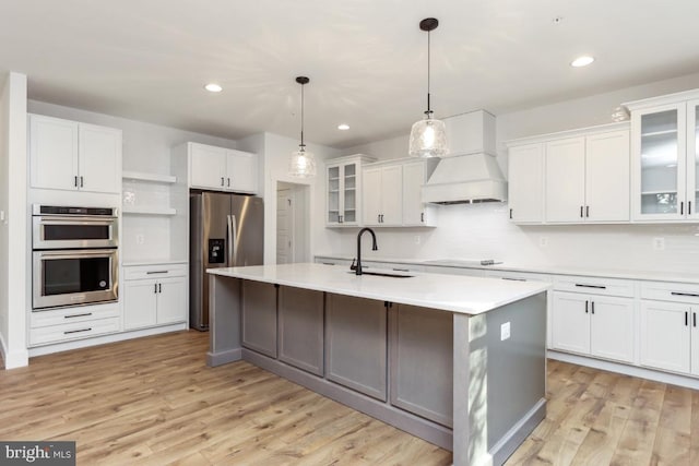 kitchen with pendant lighting, a kitchen island with sink, sink, appliances with stainless steel finishes, and custom range hood