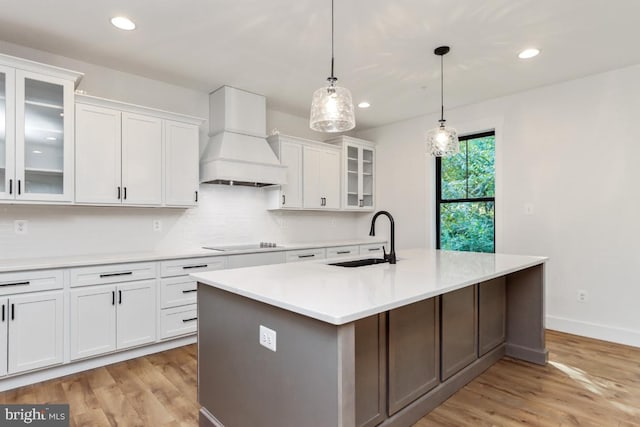 kitchen featuring sink, decorative light fixtures, a center island with sink, white cabinets, and custom range hood