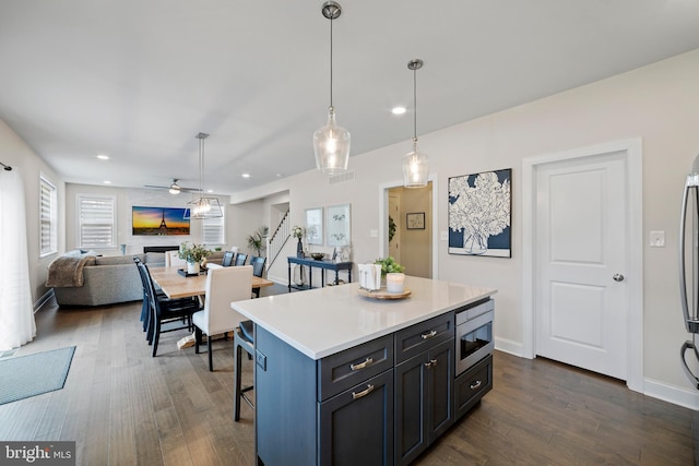 kitchen featuring ceiling fan, stainless steel microwave, a center island, decorative light fixtures, and a breakfast bar area