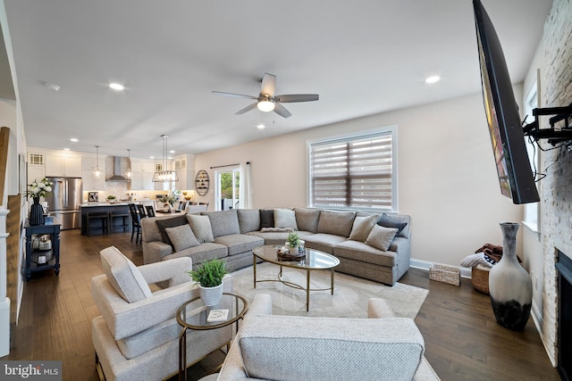 living room with ceiling fan, a stone fireplace, and dark wood-type flooring