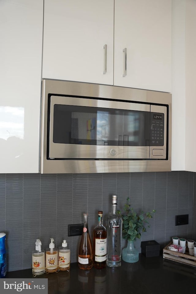 details featuring white cabinets, stainless steel microwave, and backsplash