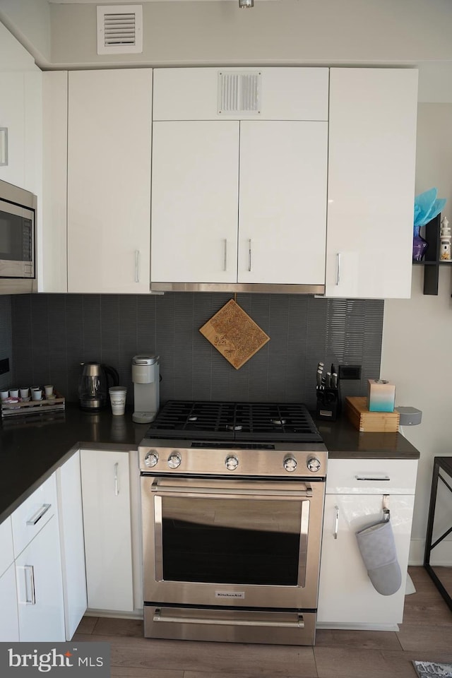 kitchen with white cabinets, appliances with stainless steel finishes, decorative backsplash, and dark hardwood / wood-style floors