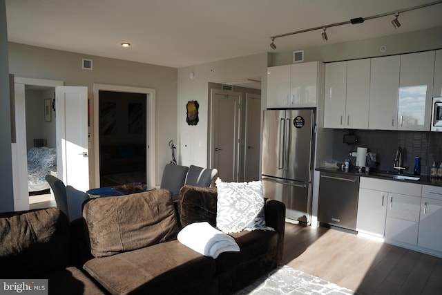 kitchen featuring sink, stainless steel appliances, track lighting, decorative backsplash, and white cabinets