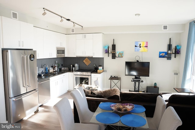 kitchen featuring light wood-type flooring, appliances with stainless steel finishes, backsplash, and white cabinetry