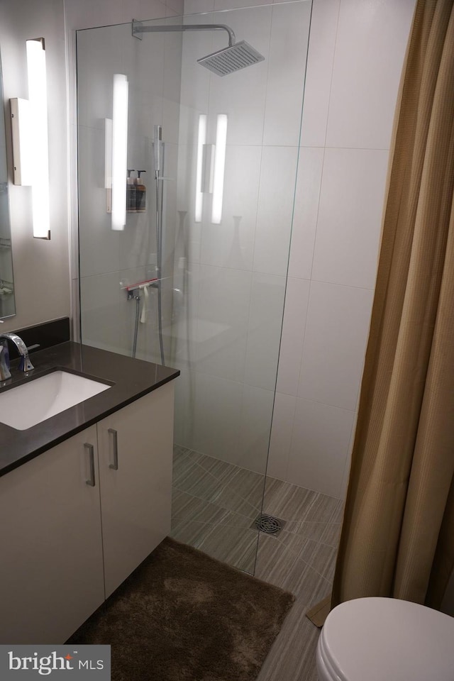 bathroom with toilet, vanity, and tiled shower