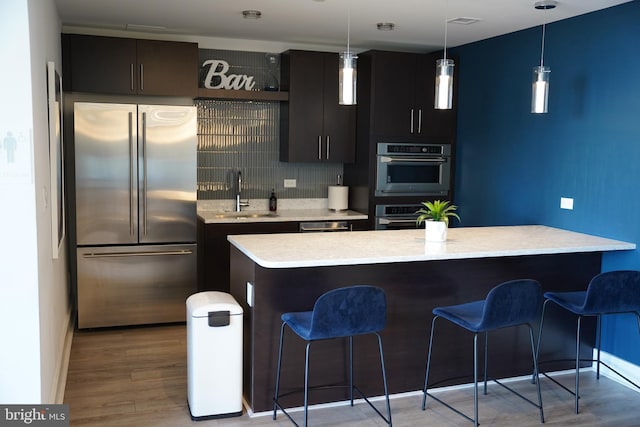 kitchen with sink, hanging light fixtures, tasteful backsplash, a kitchen island, and appliances with stainless steel finishes