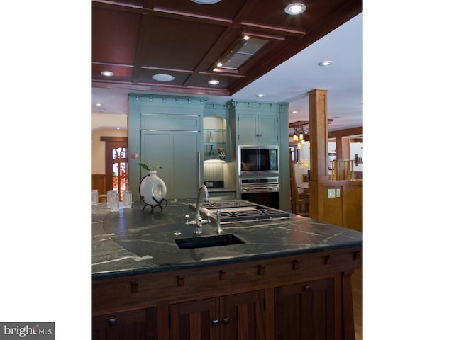 kitchen featuring ornate columns, sink, stainless steel appliances, coffered ceiling, and an inviting chandelier