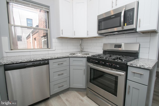 kitchen with appliances with stainless steel finishes, light hardwood / wood-style floors, white cabinetry, and sink