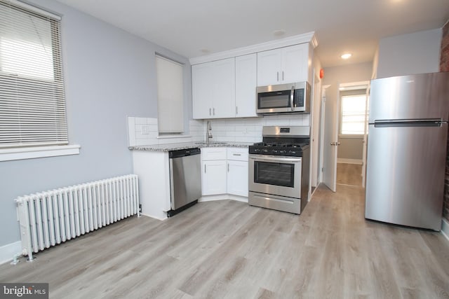 kitchen featuring white cabinets, light stone countertops, stainless steel appliances, and radiator