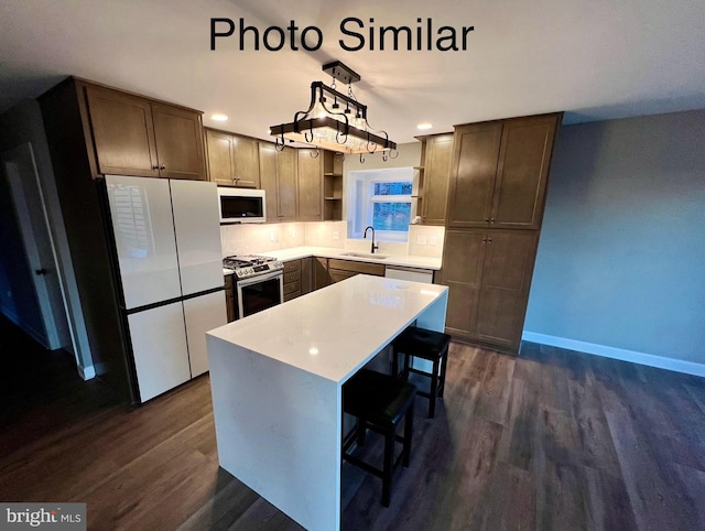 kitchen featuring white appliances, sink, a center island, dark hardwood / wood-style floors, and hanging light fixtures