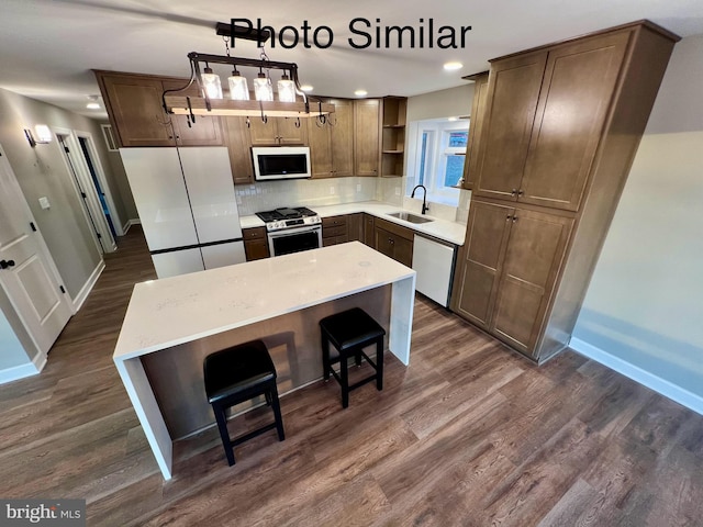 kitchen with pendant lighting, white appliances, sink, a kitchen island, and dark hardwood / wood-style flooring