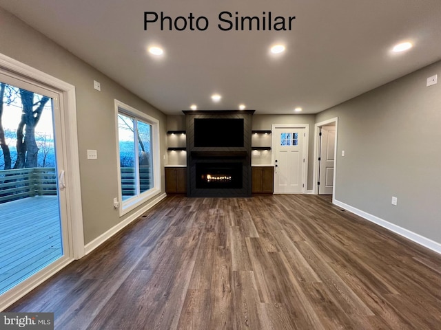 unfurnished living room featuring dark hardwood / wood-style floors, a large fireplace, and built in shelves