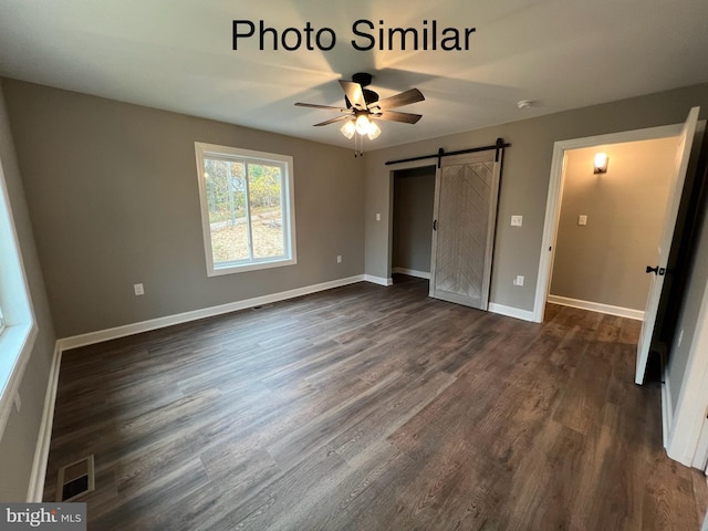 unfurnished bedroom with a barn door, ceiling fan, and dark wood-type flooring