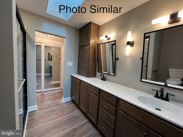 bathroom with hardwood / wood-style floors, vanity, a skylight, and toilet