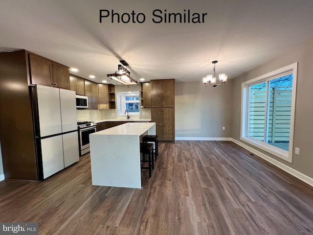 kitchen with stainless steel appliances, dark wood-type flooring, sink, a kitchen island, and hanging light fixtures