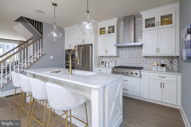 kitchen with stainless steel appliances, wall chimney range hood, a kitchen breakfast bar, an island with sink, and decorative light fixtures