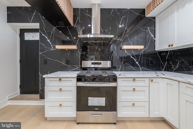 kitchen with gas range, white cabinetry, light stone countertops, light hardwood / wood-style floors, and decorative backsplash