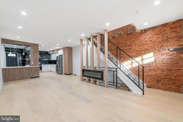 unfurnished living room with light hardwood / wood-style floors and brick wall