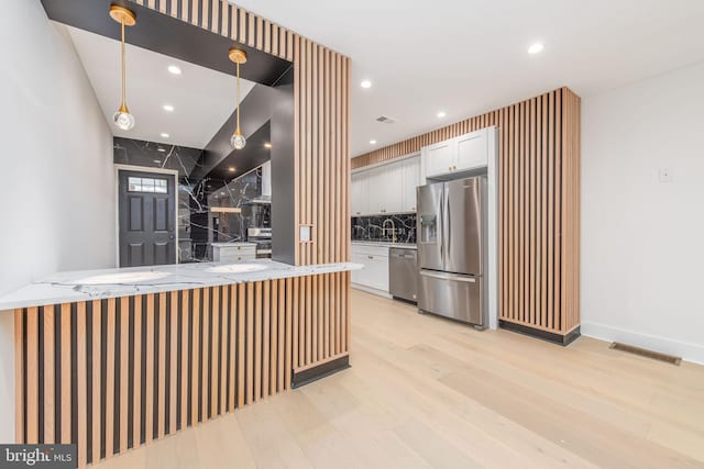 kitchen with white cabinetry, hanging light fixtures, light stone counters, and appliances with stainless steel finishes