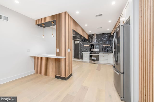 kitchen with tasteful backsplash, stainless steel appliances, wall chimney range hood, light hardwood / wood-style flooring, and white cabinetry