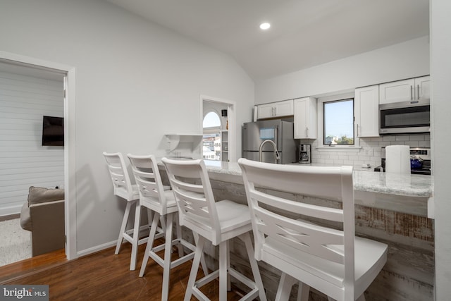 kitchen featuring backsplash, plenty of natural light, lofted ceiling, white cabinets, and appliances with stainless steel finishes