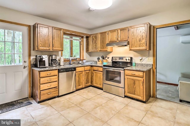 kitchen with light stone countertops, sink, stainless steel appliances, an AC wall unit, and light tile patterned floors