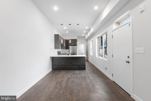 kitchen with dark brown cabinets, tasteful backsplash, kitchen peninsula, dark wood-type flooring, and appliances with stainless steel finishes