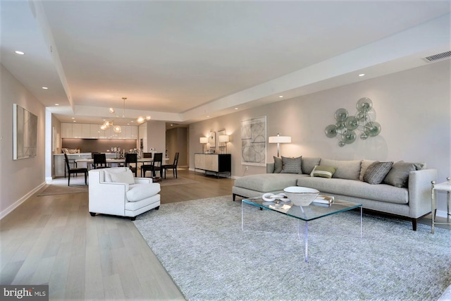 living room with hardwood / wood-style flooring, a raised ceiling, and a notable chandelier