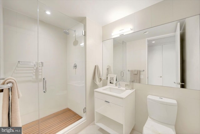 bathroom with vanity, a shower with door, toilet, and tile walls