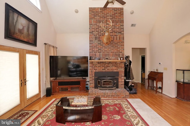 living room with a wood stove, french doors, ceiling fan, light wood-type flooring, and a towering ceiling