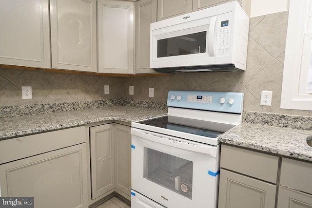 kitchen with gray cabinets, light stone countertops, white appliances, and backsplash