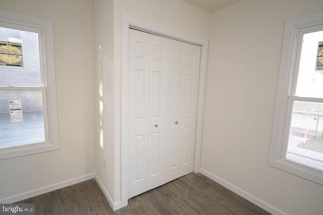 unfurnished bedroom with dark hardwood / wood-style flooring, multiple windows, and a closet