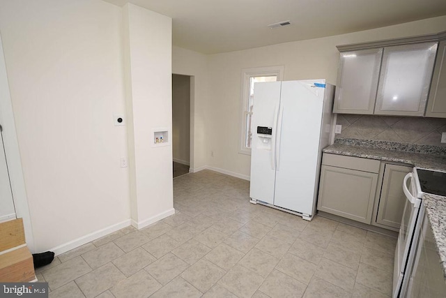 kitchen featuring gray cabinets, light stone counters, white appliances, and tasteful backsplash