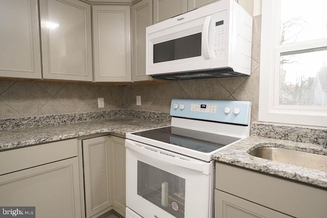 kitchen with light stone countertops, backsplash, white appliances, sink, and gray cabinets