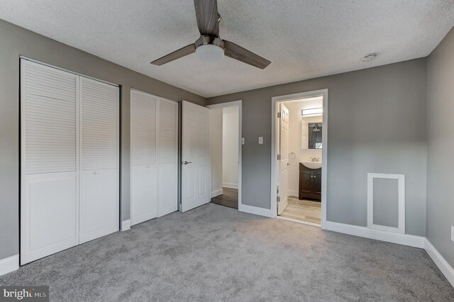 unfurnished bedroom featuring two closets, carpet, ensuite bath, and ceiling fan