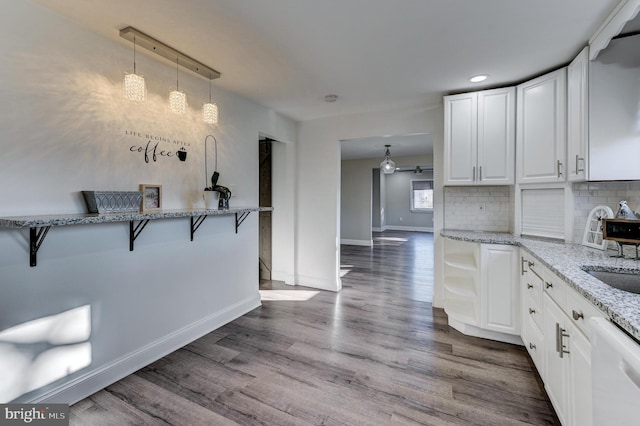 kitchen featuring a breakfast bar, backsplash, light stone countertops, dishwasher, and hardwood / wood-style flooring