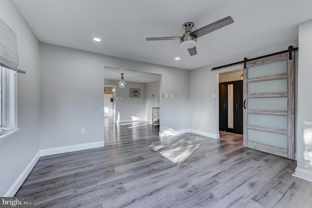 unfurnished room with ceiling fan, wood-type flooring, and a barn door