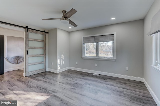 unfurnished bedroom featuring a barn door, ceiling fan, and hardwood / wood-style floors