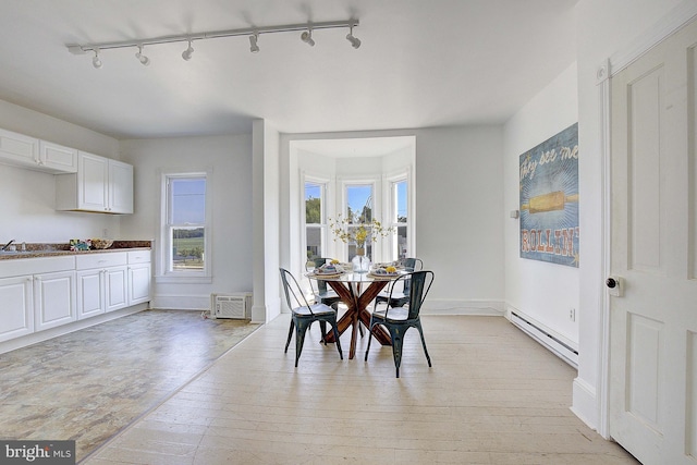 dining space featuring a wall mounted air conditioner, track lighting, sink, light wood-type flooring, and baseboard heating