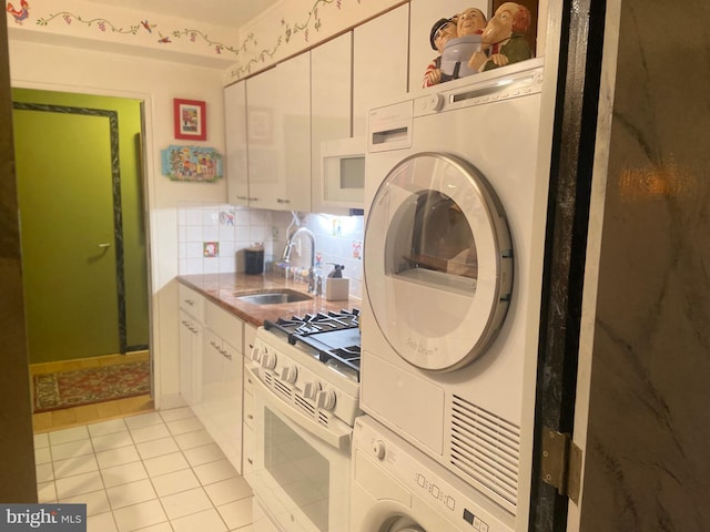 kitchen with stacked washer / dryer, tasteful backsplash, light tile patterned floors, white appliances, and sink