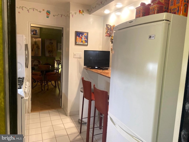 kitchen featuring a breakfast bar area, white refrigerator, and light tile patterned floors