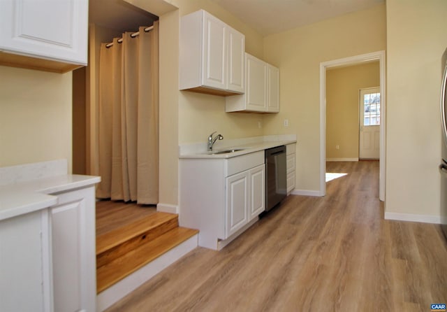 kitchen with stainless steel dishwasher, white cabinets, sink, and light hardwood / wood-style flooring