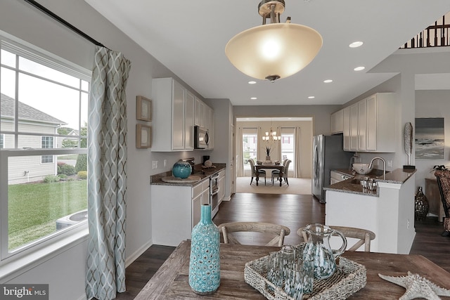 kitchen with an inviting chandelier, a sink, dark wood-type flooring, white cabinets, and appliances with stainless steel finishes