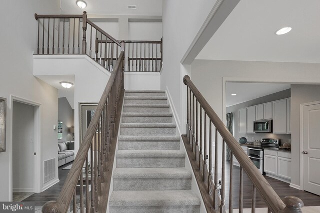 stairs with visible vents, recessed lighting, a high ceiling, and wood finished floors