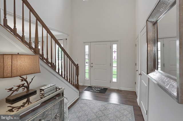 foyer entrance with stairway, baseboards, a towering ceiling, and wood finished floors