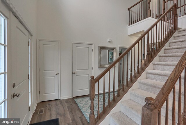entrance foyer with stairway, a high ceiling, visible vents, and wood finished floors