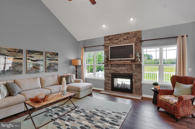 living room featuring high vaulted ceiling, wood finished floors, a stone fireplace, baseboards, and ceiling fan