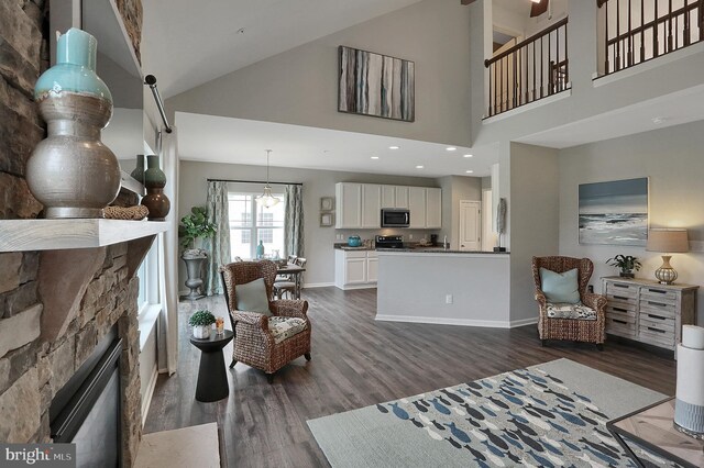 living room with high vaulted ceiling, recessed lighting, a stone fireplace, baseboards, and dark wood-style flooring